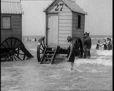 Female Civilian in Bathing Suit Standing in the Sea Watching Changing Cabins on Wheels Being...,1924 Creator: British Pathe Ltd