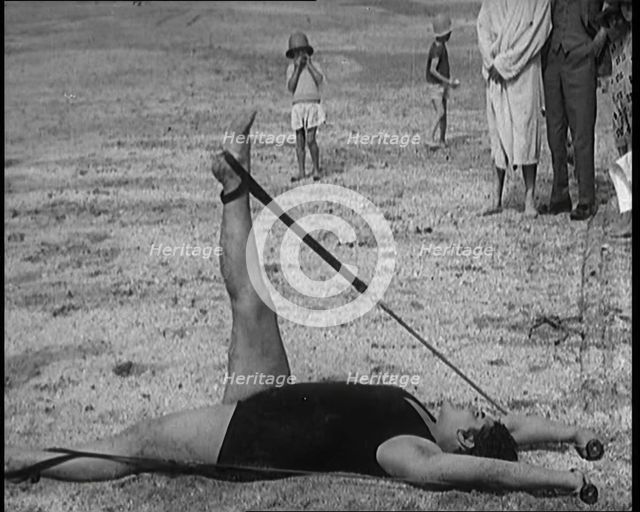Female Civilian Laying on the Sand Exercising with an Elastic Band on a Beach, 1920. Creator: British Pathe Ltd.