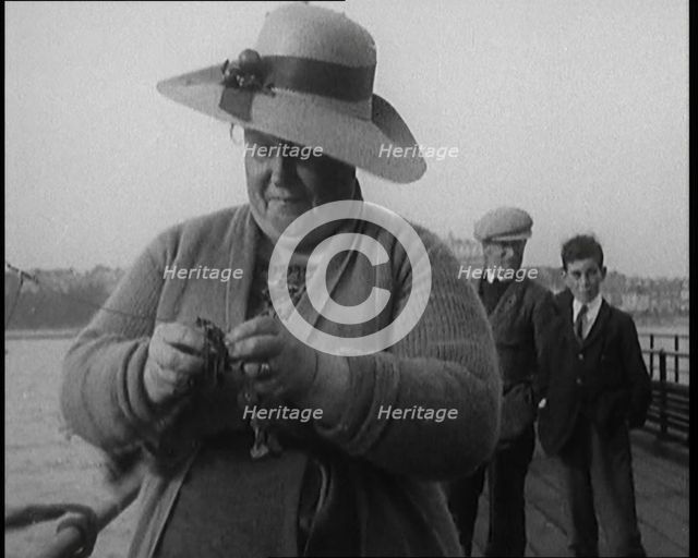 Female Civilian Removing Seaweed from a Fishing Hook Whilst Fishing from a Pier, 1920. Creator: British Pathe Ltd.
