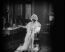 Female Civilian Seating in Front of a Dressing Table Wearing a Nightgown and Boudoir Cap, 1920. Creator: British Pathe Ltd