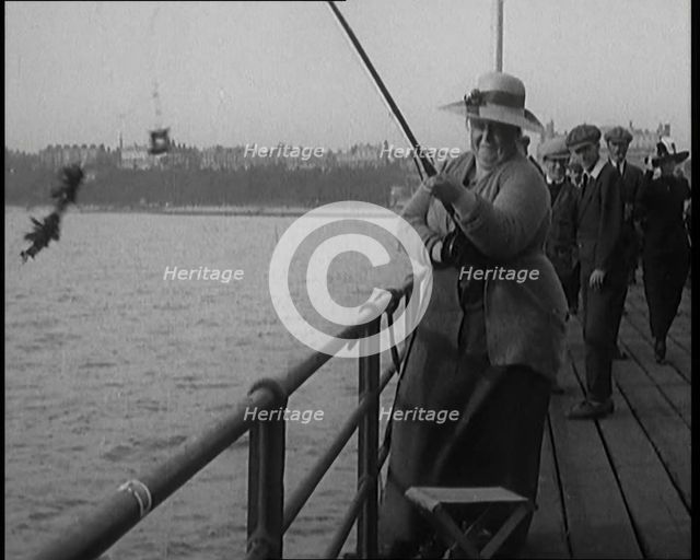 Female Civilian Wearing a Hat with a Dark Ribbon Fishing from a Pier, 1920. Creator: British Pathe Ltd.