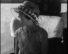 Female Civilian Wearing a Large Fashionable Hat Decorated with Flowers Seating at the Window...1920. Creator: British Pathe Ltd