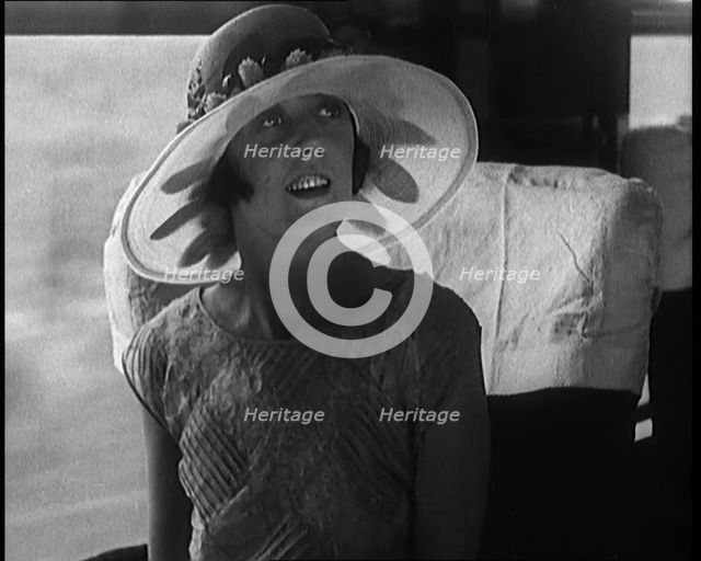 Female Civilian Wearing a Large Fashionable Hat Decorated with Flowers Seating at the Window...1920. Creator: British Pathe Ltd.