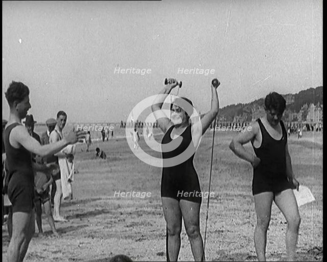 Female Civilian Wearing a Swimsuit Exercising with Elastic Bands on a Beach, 1920. Creator: British Pathe Ltd.