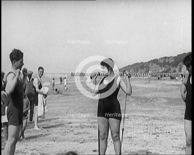 Female Civilian Wearing a Swimsuit Exercising with Elastic Bands on a Beach, 1920. Creator: British Pathe Ltd.