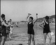 Female Civilian Wearing a Swimsuit Exercising with Elastic Bands on a Beach, 1920. Creator: British Pathe Ltd