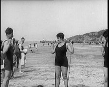 Female Civilian Wearing a Swimsuit Exercising with Elastic Bands on a Beach, 1920. Creator: British Pathe Ltd