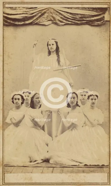 Female group portrait, six in white gowns kneeling, one standing holding a cross, about 1865. Creator: Unknown.