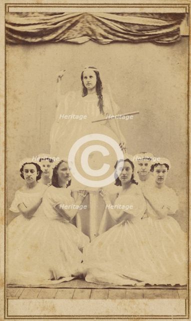 Female group portrait, six in white gowns kneeling, one standing holding a cross, about 1865. Creator: Unknown.