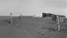 Fence corner and outbuilding being buried by dust, Mills, New Mexico, 1935. Creator: Dorothea Lange