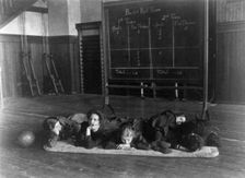 Five girls lying on mat in gymnasium in front of basketball scoreboard..., Washington, D.C., (1899?) Creator: Frances Benjamin Johnston