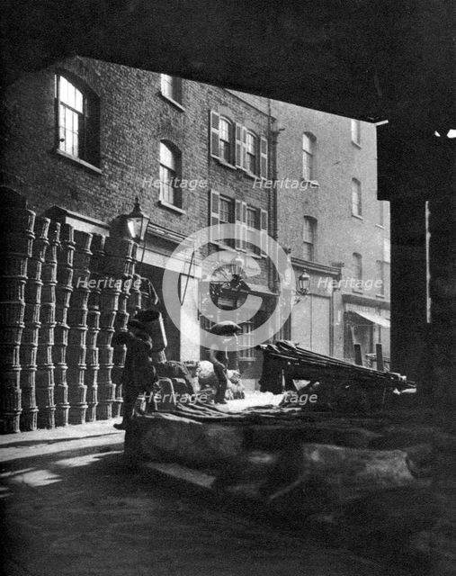 Fruit baskets piled against houses at Borough Market, London, 1926-1927.Artist: Whiffin