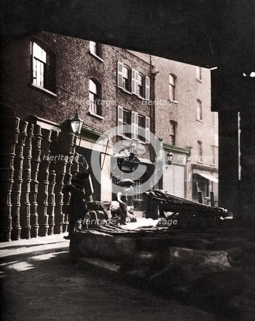 Fruit baskets piled against houses at Borough Market, London, 1926-1927. Artist: Whiffin.