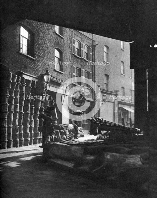 Fruit baskets piled against houses at Borough Market, London, 1926-1927.Artist: Whiffin