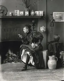 Frances Benjamin Johnston, full-length portrait, seated in front of fireplace, facing left..., 1896. Creator: Frances Benjamin Johnston