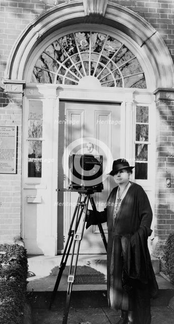 Frances Benjamin Johnston, full-length portrait, standing in front of door, with camera..., c1935. Creator: Unknown.