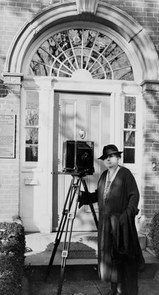 Frances Benjamin Johnston, full-length portrait, standing in front of door, with camera..., c1935. Creator: Unknown
