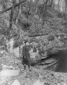 Frances Benjamin Johnston, full, standing by wooded cliff at entrance to Mammoth Cave, (c1891?). Creator: Frances Benjamin Johnston
