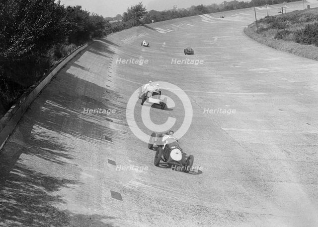 Freddie Dixon's Riley Red Mongrel Special leading RJ Munday's Munday Special, Brooklands, 1933. Artist: Bill Brunell.