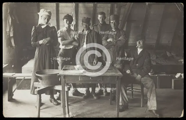 French prisoners of war, one in drag, gather round a small wooden table, [between 1910 and 1919?]. Creator: Unknown.