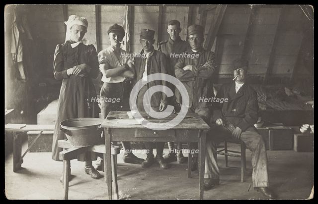French prisoners of war, one in drag, gather round a small wooden table, [between 1910 and 1919?]. Creator: Unknown.