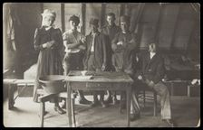 French prisoners of war, one in drag, gather round a small wooden table, [between 1910 and 1919?]. Creator: Unknown
