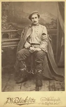 Full-length portrait of a man in convict clothing and leg irons, seated..., between 1880 and 1886. Creator: Unknown
