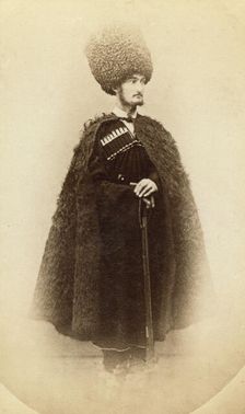 Full-length portrait of a man in cape and sheep skin hat, holding a rifle..., between 1870 and 86. Creator: Unknown