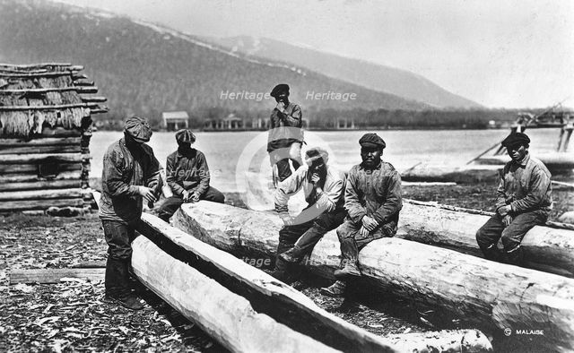Kamchadals on the river bank near the baht and logs prepared for hollowing out the baht, 1922-1923. Creator: Rene Malaise.