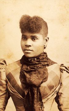 Half-portrait of young woman wearing large lace scarf over plaid bodice, c1880-c1889. Creator: James O Durgan