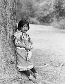 Innocence, an Umatilla girl, full-length portrait, standing by tree, facing slightly right, c1910. Creator: Edward Sheriff Curtis