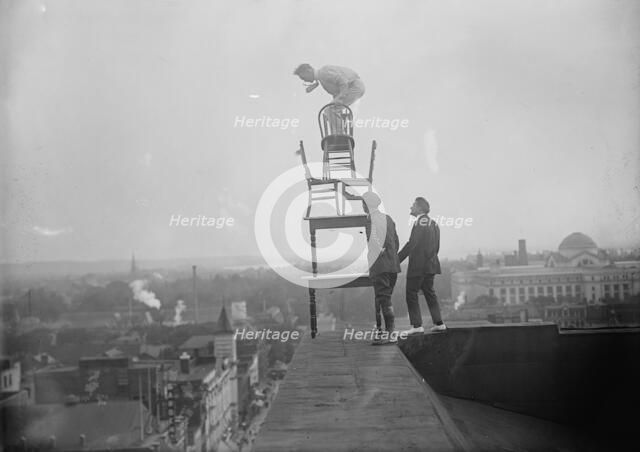 J. Reynolds, Performing Acrobatic And Balancing Acts On High Cornice Above 9th Street, N.W., 1917. Creator: Harris & Ewing.
