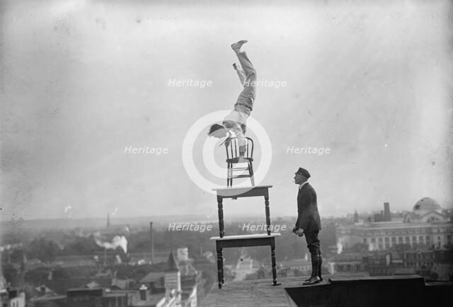J. Reynolds, Performing Acrobatic And Balancing Acts On High Cornice Above 9th Street, N.W., 1917. Creator: Harris & Ewing.