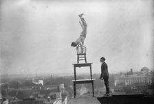 J. Reynolds, Performing Acrobatic And Balancing Acts On High Cornice Above 9th Street, N.W., 1917. Creator: Harris & Ewing