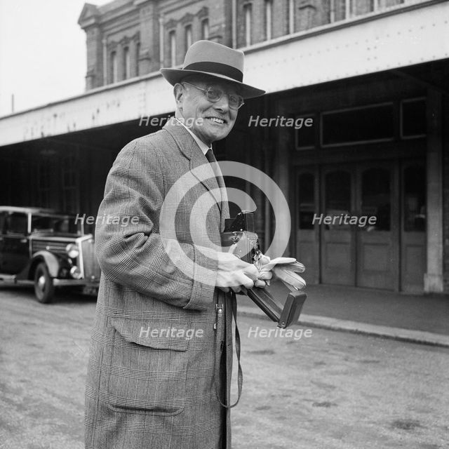 John Laing holding a Rolleiflex camera outside Bournemouth train station, 30/05/1953. Creator: John Laing plc.