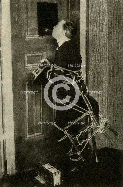 John Nevil Maskelyne performs a 'spirit cabinet illusion', c1910. Creator: Unknown.