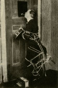 John Nevil Maskelyne performs a spirit cabinet illusion c1910. Creator: Unknown