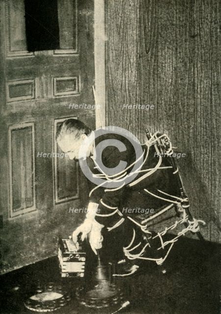 John Nevil Maskelyne performs a 'spirit cabinet illusion', c1910. Creator: Unknown.