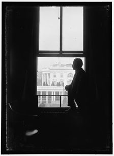 John Skelton Williams at window with White House visible in background..., between 1913 and 1918. Creator: Harris & Ewing