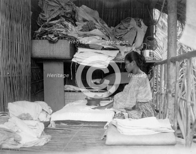 Javanese(?) woman sitting in room working with textiles at exhibit featuring foreign..., 1892. Creator: Frances Benjamin Johnston.