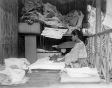 Javanese(?) woman sitting in room working with textiles at exhibit featuring foreign..., 1892. Creator: Frances Benjamin Johnston