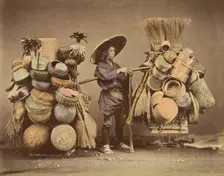 [Japanese Man Posing with Baskets, Brooms and Feather Dusters], 1870s. Creator: Unknown