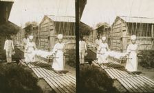 Japanese nurses carrying a patient on a stretcher, c1905. Creator: Underwood & Underwood