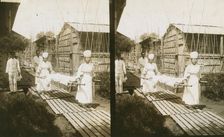Japanese nurses carrying a patient on a stretcher, c1905. Creator: Underwood & Underwood