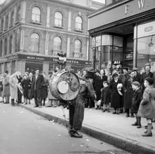 One-man band performing in front of a crowd outside Woolworths, Camden, London, 1952. Creator: Henry Grant
