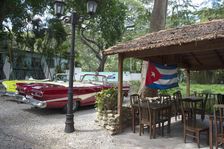 Old American cars and the Cuban flag at the Bosque, Havana, Cuba, 2024. Creator: Ethel Davies