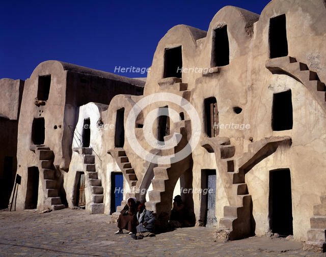 Old typical barns with people sitting on the stairs.