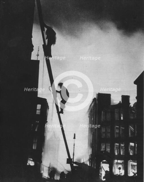 'Out in the Blitz, silhouetted aganinst the light of fires, rescue men climb into a building in St.  Artist: Unknown.