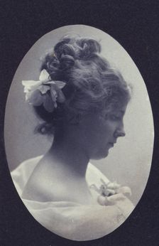 Oval portrait of woman with a flower in her hair and a corsage on her dress, c1900. Creator: Fannie L. Elton
