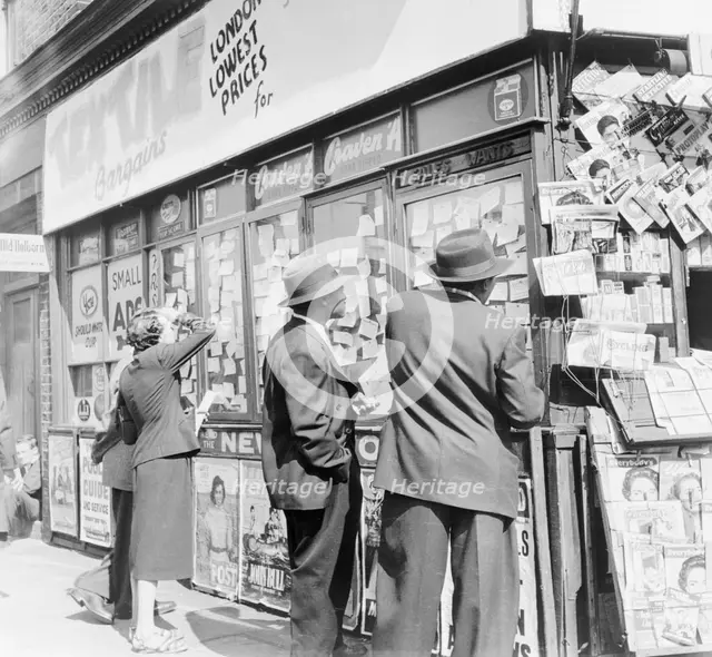 Looking at accomodation notices and job vacancy advertisements in a newsagents window, c1955. Creator: Henry Grant.